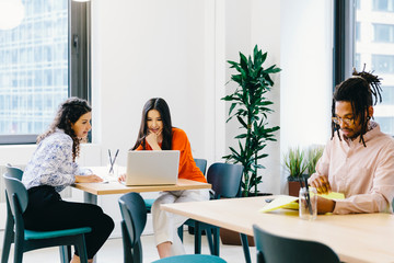 Businessman reading documents while female colleagues discussing over laptop computer in office