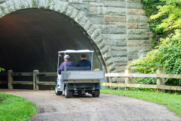 Golf cart on dirt path going under a bridge