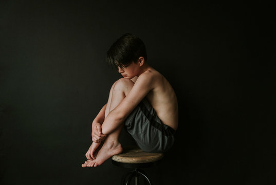 Side view of shirtless boy sitting on stool