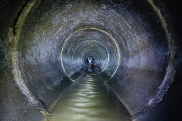 Diggers (urban explorers) are exploring underground river flowing in round sewer tunnel - obrazy, fototapety, plakaty