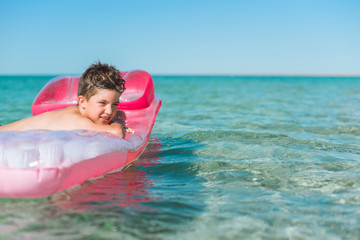 Cheerful boy swims in the sea on a inflatable mattress.