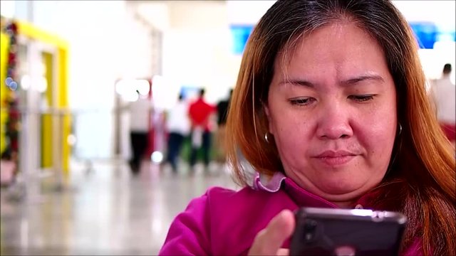 Hand held video shot of an Asian woman using her smartphone to pass the time at an airport's waiting area.