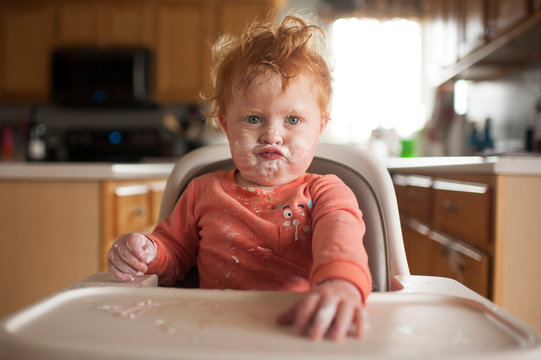 Boy with messy face puckering lips on high chair at home