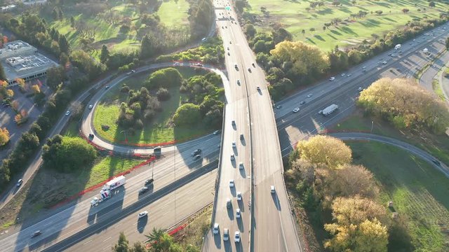 Aerial view late in the afternoon above a freeway and golf course with cars and on ramp circles below.