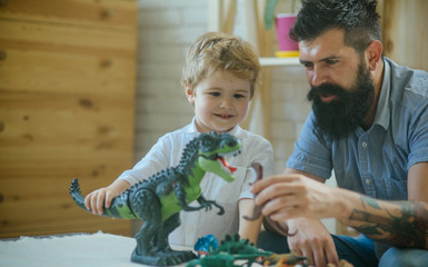 Kid and bearded man play fight between kid's toys on the wood table, different dinosaurs. Educating...