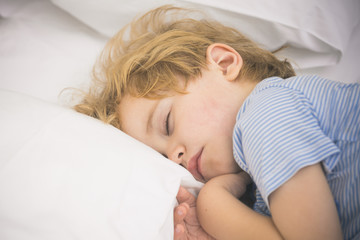 Adorable blond child is sleeping on pillow. Comfortable bed and healthy dream for children. Boy in pajamas and hypoallergenic bedding. Portrait of beloved son taking nap. Cosy and delicate bedding.