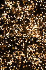 Blurry golden and white fairy lights in dark night creating beautiful bokeh effect with glowing...
