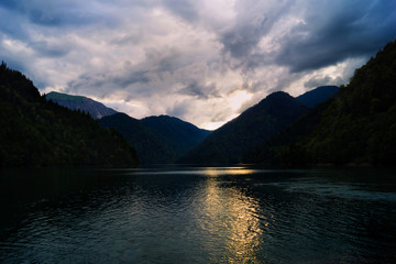 Sunset on a mountain lake. Alpine pond. Dark low clouds. Reflection of the sun in the water.