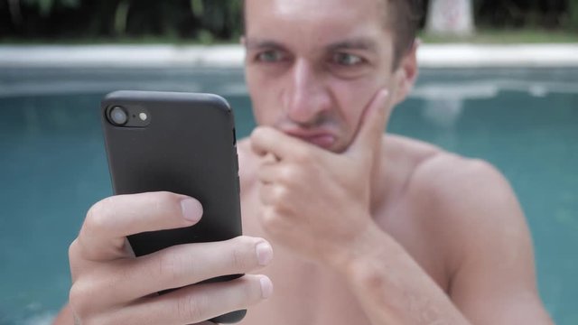 Angry man aggressively uses smartphone outdoor in the swimming pool on vacation.