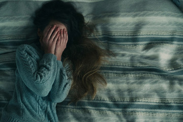 High angle view of girl with hands covering face while lying on bed at home