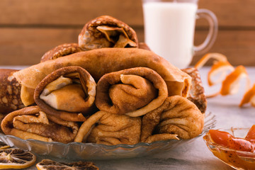 Rolled pancakes. Wooden light background. Milk in glass.