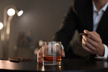 Man with glass of whiskey and cigar sitting at table, closeup. Space for text