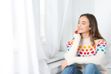 Obraz na płótnie Canvas Beautiful teenage girl in warm cozy sweater looking out window at home. Space for text