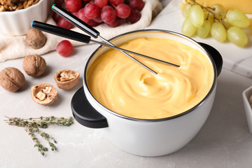 Pot of delicious cheese fondue and forks on gray table