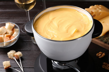 Pot with delicious cheese fondue on wooden table