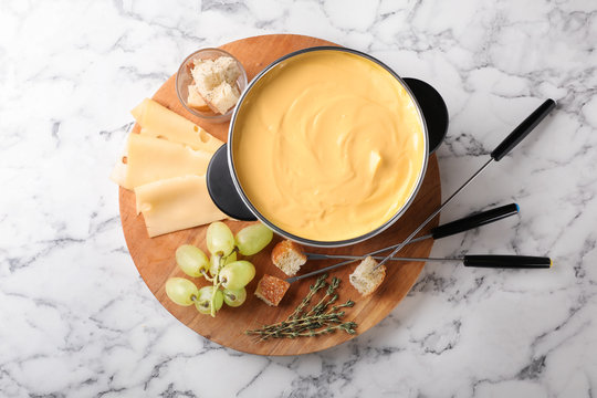 Flat lay composition with pot of delicious cheese fondue on marble table