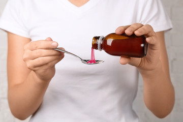 Woman pouring cough syrup into spoon, closeup