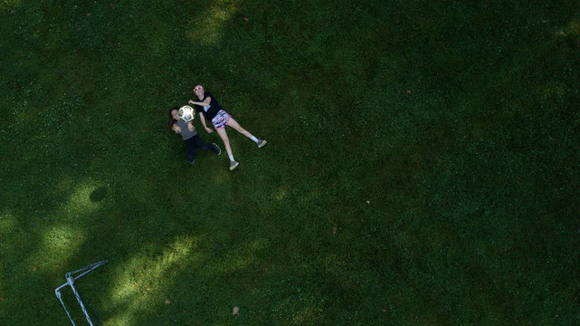 High angle view of sisters playing with ball while lying on grassy field at park