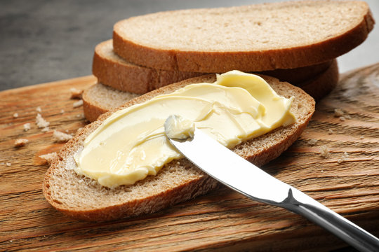 Spreading butter onto toast with knife on wooden board