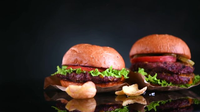 Hamburger and double cheeseburger with fries rotated on black background. Cheeseburgers served with french fries. 4K UHD video footage. 3840X2160