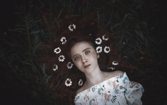 High angle portrait of teenage girl with chamomiles lying on grassy field