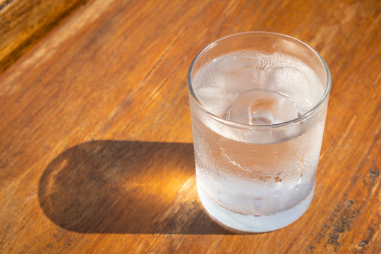 glass of water with ice cubes on wooden table