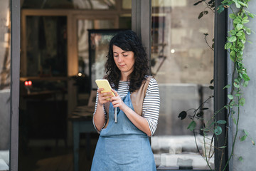 Confident female artisan using smart phone while standing by door at workshop
