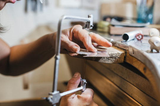 Cropped hands of female artisan using handsaw while making jewelry on wooden table in workshop - Powered by Adobe
