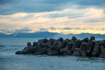 秋の終わりの朝、日本海の夜明けに波がテトラポットに打ち付けられ、波飛沫が泡立つ光景が美しい。