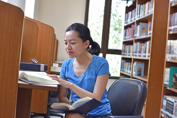 Asian woman doing research and reading book in public library.