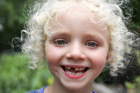Close-up portrait of happy girl with messy blond hair standing at yard