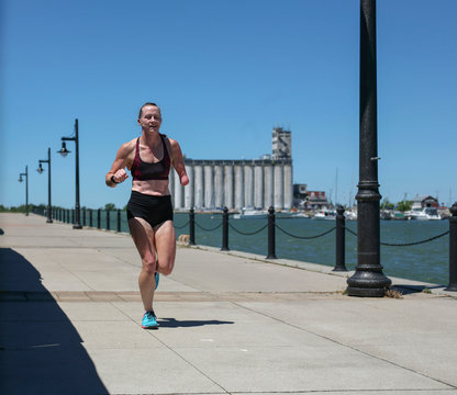Female athlete running by lake on footpath against clear blue sky