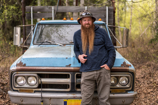 Portrait of bearded man leaning on old pickup truck in forest
