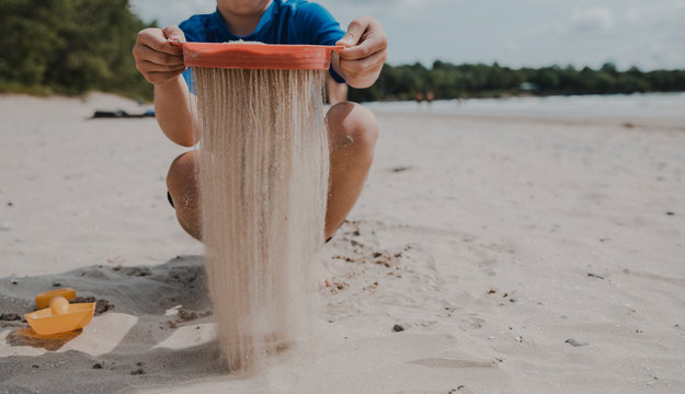 Low section of boy sieving sand while crouching at beach