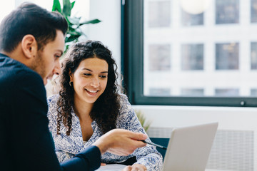 Businessman explaining data to female colleague over laptop computer in office