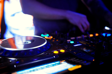 Naklejka premium Disc Jockey mixing deck and turntables at night with colourful illuminated controls for mixing music for a party or disco