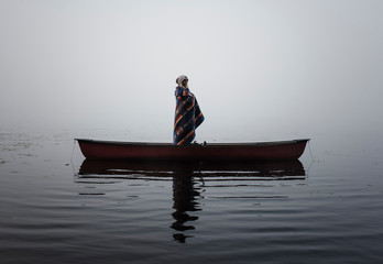 Woman with blanket standing in boat on river during foggy weather
