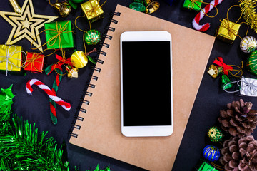 Top view image of Christmas festive decorations with empty smartphone,notebook and pencil on black paper background, New Year concept.