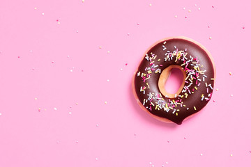 Overhead view of chocolate donut with sprinkles on pink background