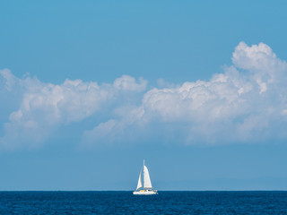 White sailing boat on the horizon with clouds in the background