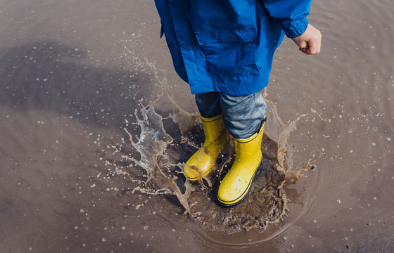 Low section of playful boy wearing yellow rubber boots while splashing puddle