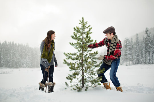 Happy couple standing by pine tree on snow covered field against sky in forest