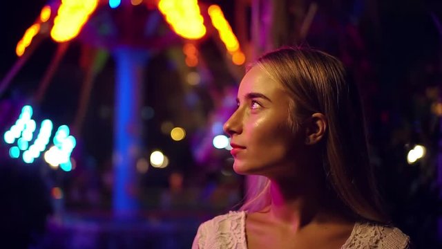 Attractive long-haired blonde young caucsian girl happily smiles look to camera city lights on the background portrait device beauty technology fashion girl dark tourism tourist urban slow motion