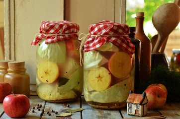 Pickled pieces of cabbage and apples in glass jars on a wooden background