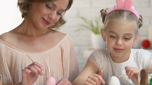 Friendly daughter and mother in headbands having fun painting nose to each other