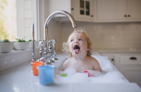 Shirtless girl drinking water from faucet in sink at home