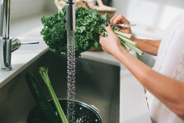 A woman washing vegetables in the kitchen sink. 
