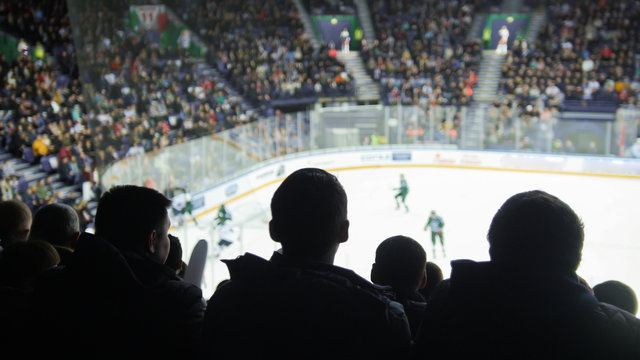 A group of silhouettes of young people watching hockey match in a closed stadium