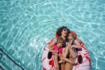 High angle view of happy mother with daughters lying on inflatable ring in swimming pool at tourist resort