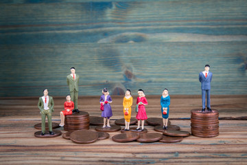 Miniature people standing on piles of coins. Income and economic inequality concept